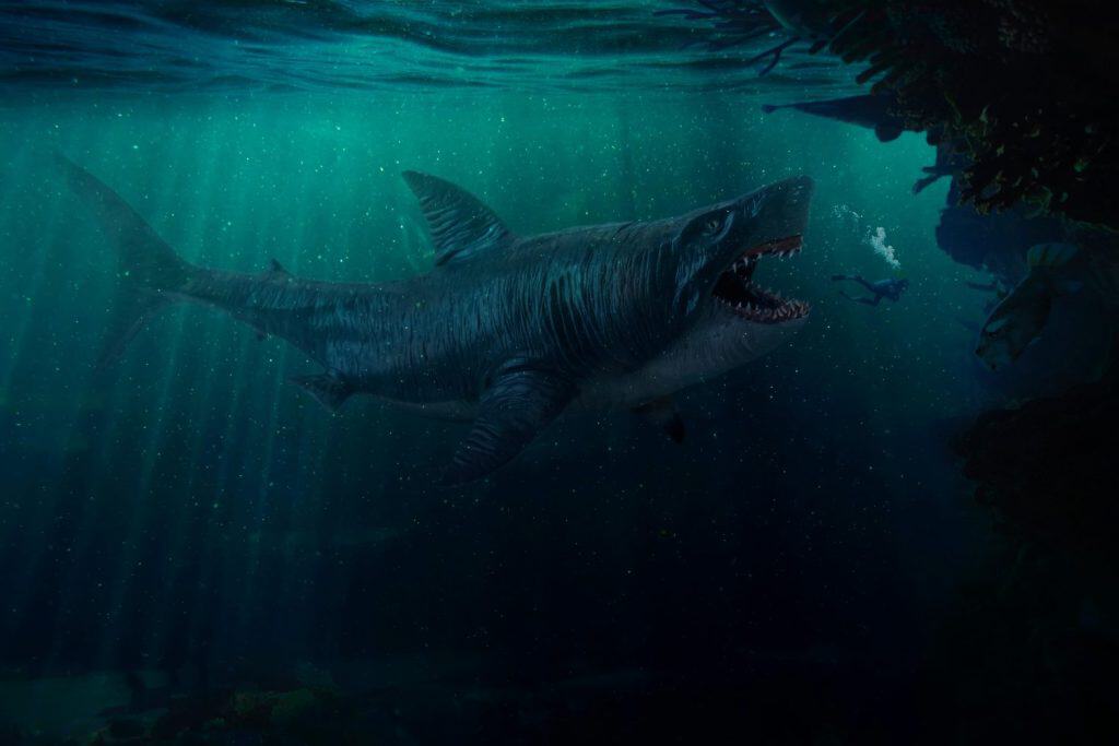 Ancient evil megalodon with open mouth full of sharp teeth attacks scuba diver in dark blue sea. Man tries to escape the monster in panic by releasing air bubbles. Сoral reef in foreground on right