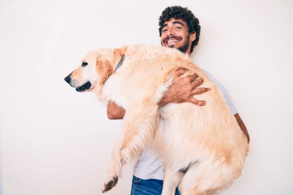 Young handsome man holding and hugging labrador retriever dog, smiling with love to his best friend