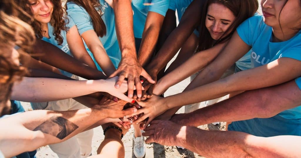 People of different ages and races are united to protect environment from pollution. Happy volunteers stacking hands together to cheer and boost team spirit. Friendship, teamwork, volunteering.