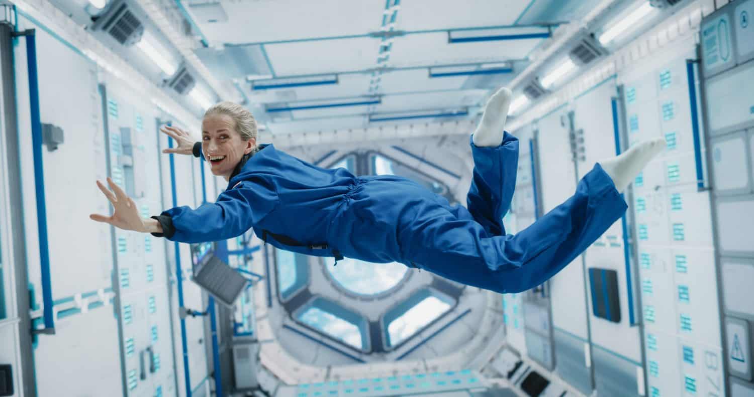 Portrait of a Courageous Caucasian Female Astronaut on Board a Spacecraft, Floating in Zero Gravity and Smiling At The Camera. Space Travel, Solar System Exploration and Colonization Concept