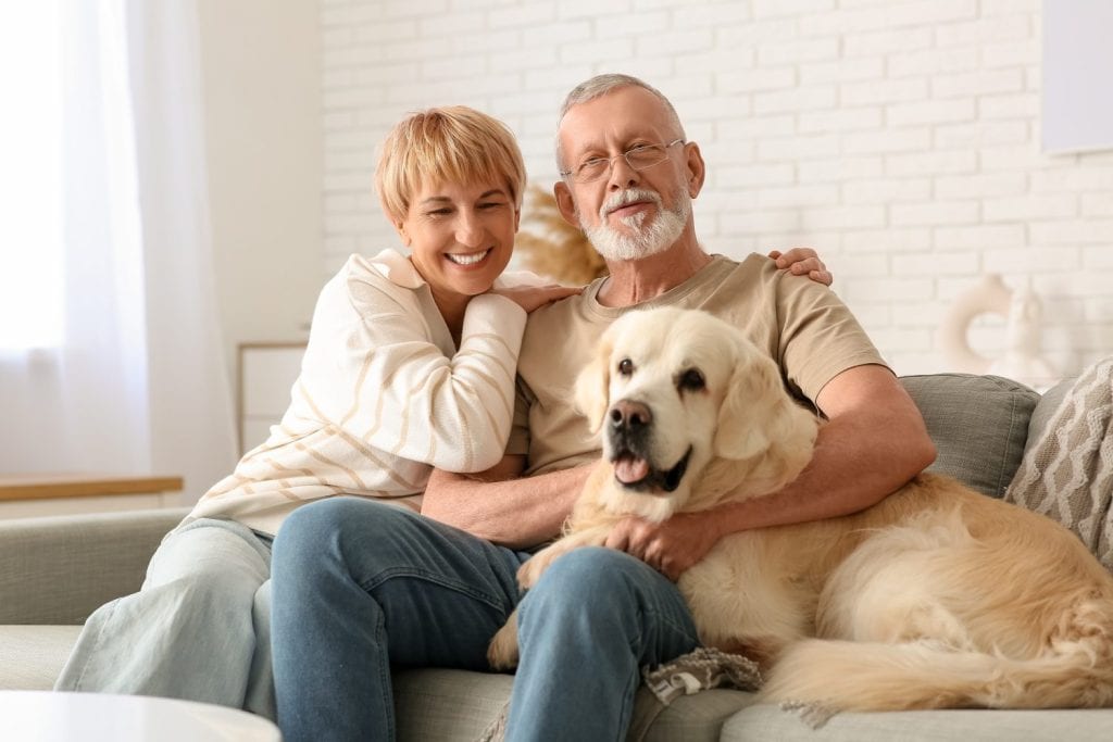 Mature couple with Labrador dog sitting on sofa at home