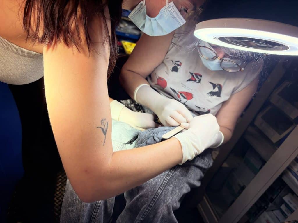 women bent over in surgical masks doing something with a bird and popsicle stick