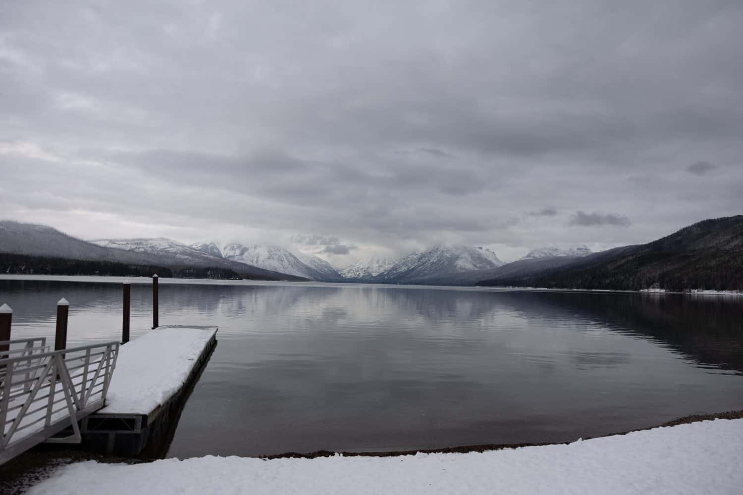 Montana lake McDonald in the national glacier park during winter with snow. Clear blue ice water with colorful stones with beautiful reflection.