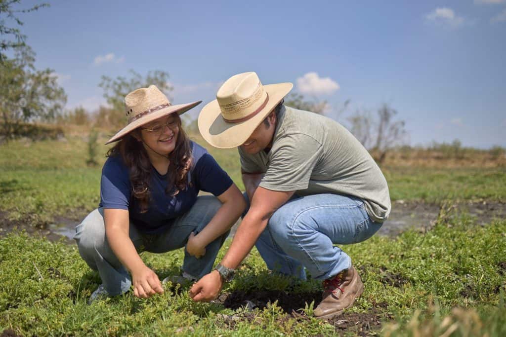 Two volunteers smile while picking up trash in the wetlands of Xochimilco, working together to protect the local ecosystem