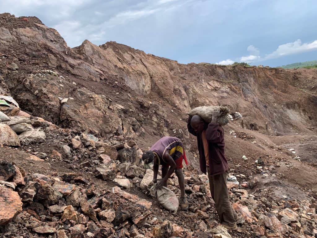 a couple of young men hauling sacks of rocks on a rubbled hillside.
