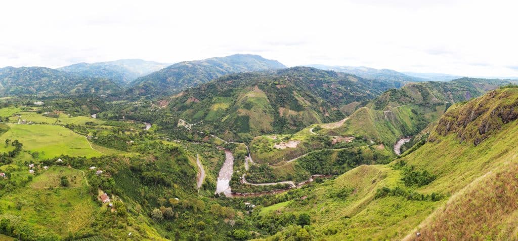 Vista with green hills that look grazed around a river with a background of low moutains.