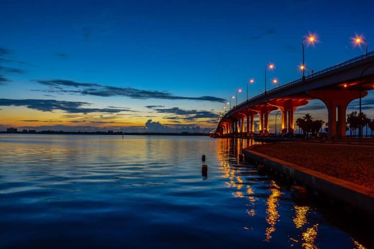 The sun coming up over the Indian River lagoon in Florida with a causeway bridge lit with street lights making golden reflections in the rippled water