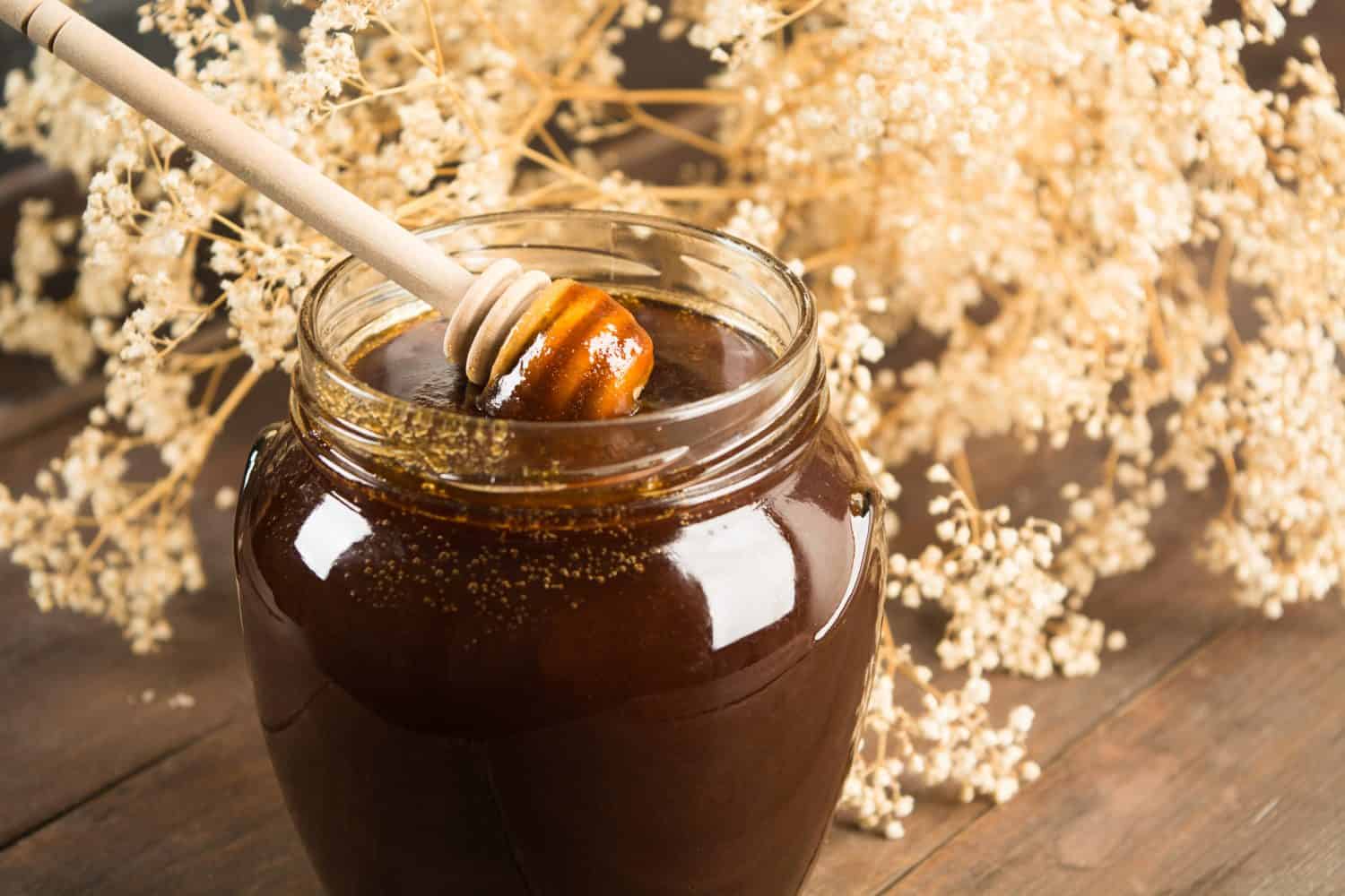 Closeup of dark honey with spoon with flowers on background
