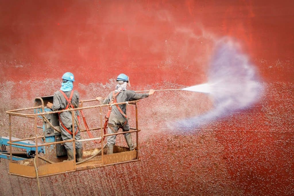 Worker two man with safety harness and protective by pressure washer cleaning ship on Trucks have sherry piker, the success of the work in shipyard Thailand
