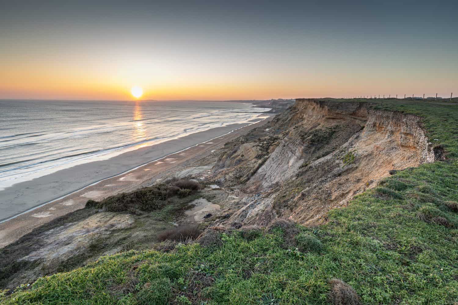 Coastal cliffs with a low sun at sunset showing sea, low tide sand bars, erosion and near Barton-on-Sea, Hampshire, UK