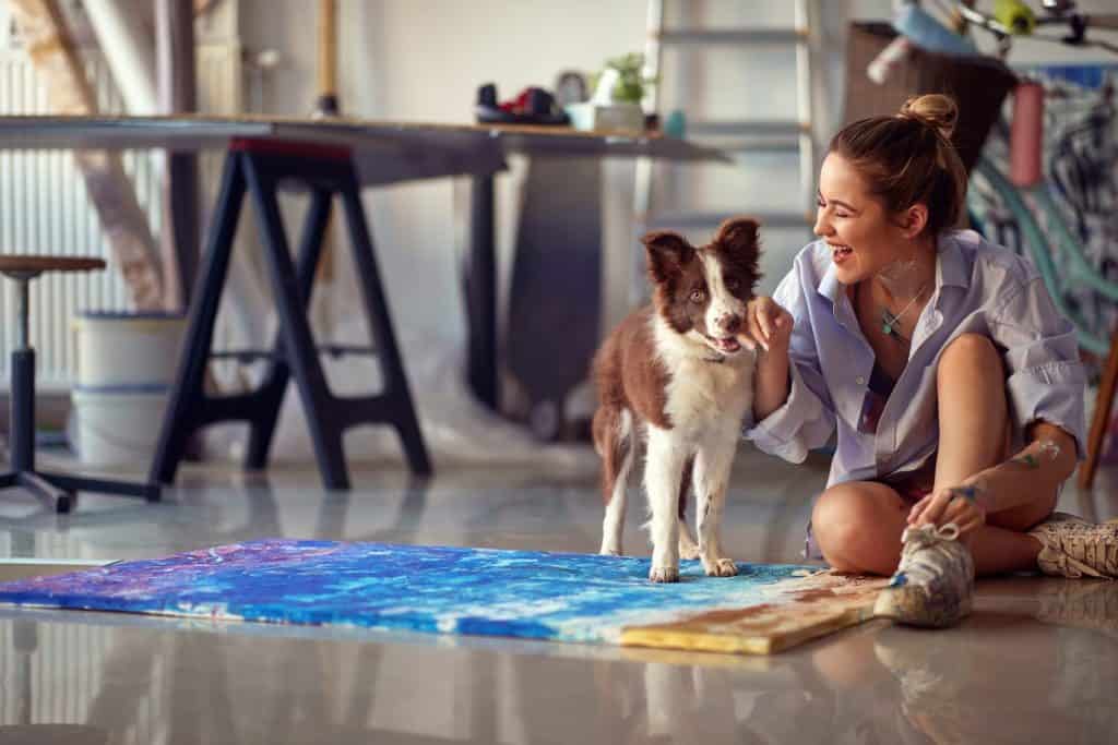Young attractive female artist playing with her dog in the studio