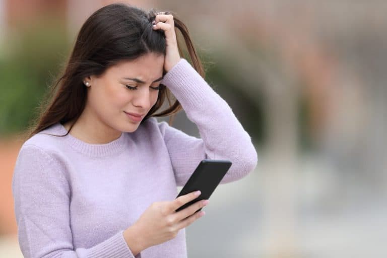 Sad teen complaining reading smart phone text standing in the street