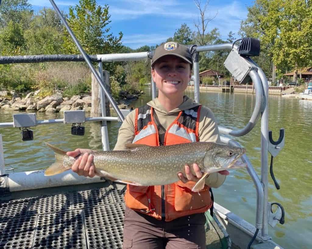 woman wearing orange vests holds up fish that appears to be about two feet long.