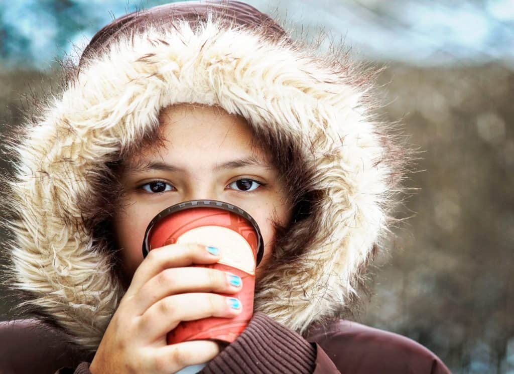Indigenous Metis young girl, warm winter coat, furry hood up, drinking hot chocolate take out. Canadian, eh? Cold weather, drink, beverage. Outside outdoors. Season seasonal. Canada. Warming up.