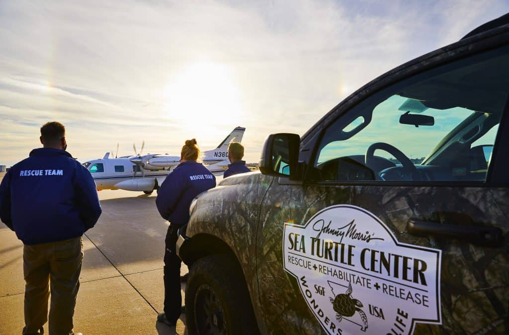 people with rescue team jackets face a small plane while leaning on a truck with SEA TURTLE CENTER logo.