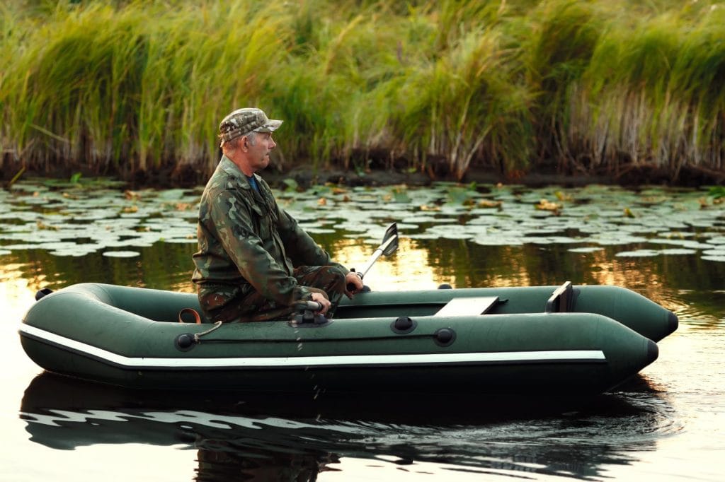 An elderly man is sailing on a rubber boat with oars on a calm river. The inspector checks the reservoir from poachers and intruders. The concept of environmental protection from pests.