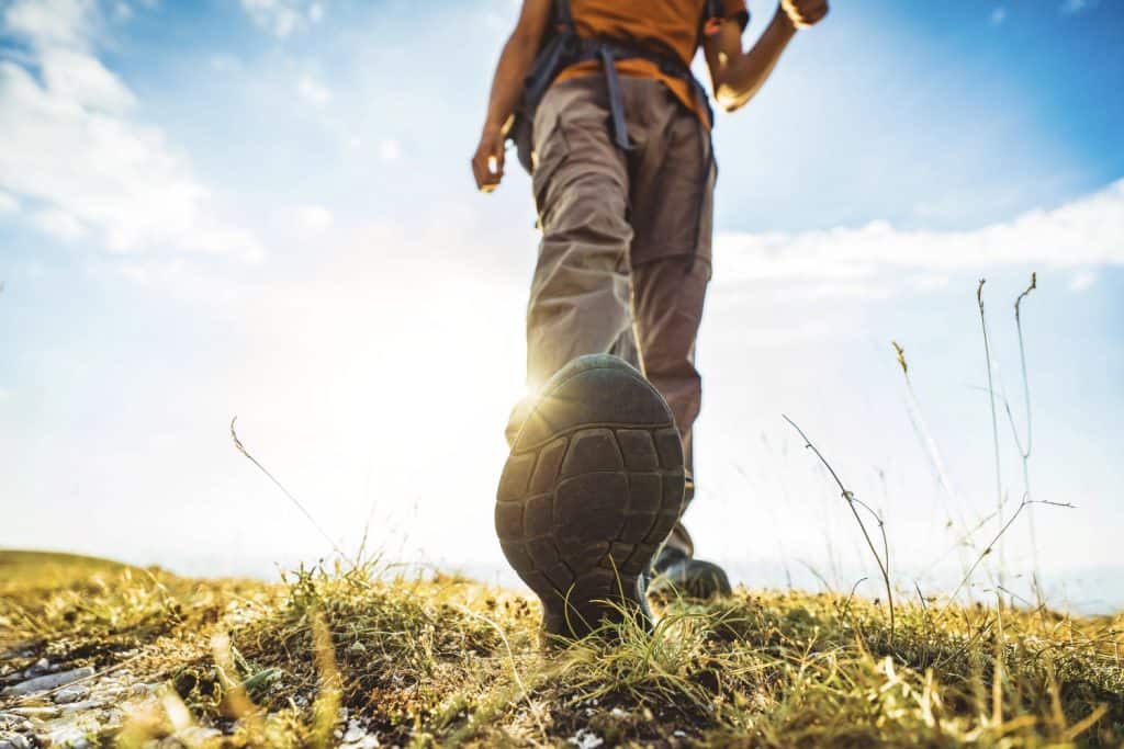 Close-up photo of male legs in trekking boots walking on a hiking trail - Happy hiker climbing mountains - Travel and sport life style concept
