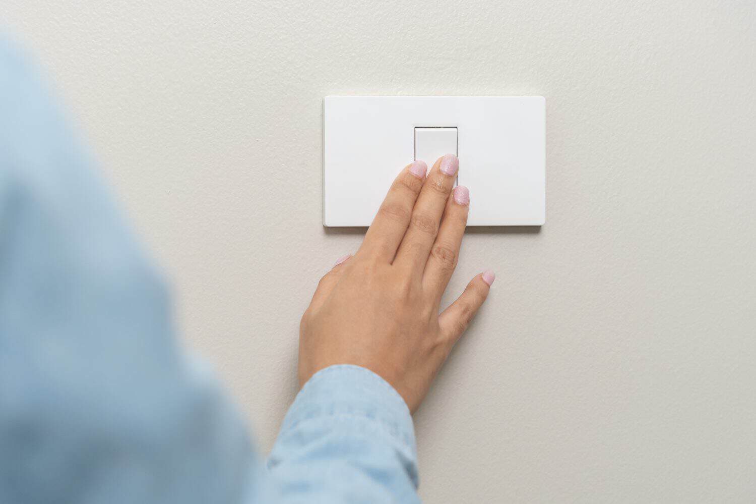 Asian young woman hand turn off on lighting switch at home room. Finger pushing light switch turn on or off white switch on wall for saving, control power electrical energy, eco environment concept.
