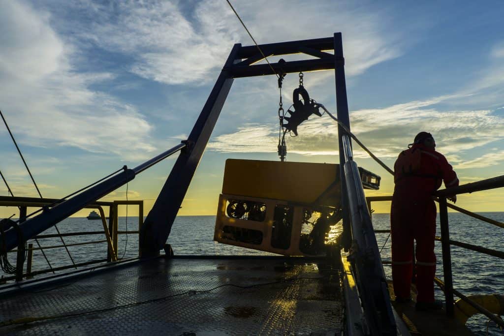 Silhouette of worker recovering robotics Remote Operated Vehicle (ROV) after entering sea surface during oil and gas pipeline inspection in the middle of South China Sea