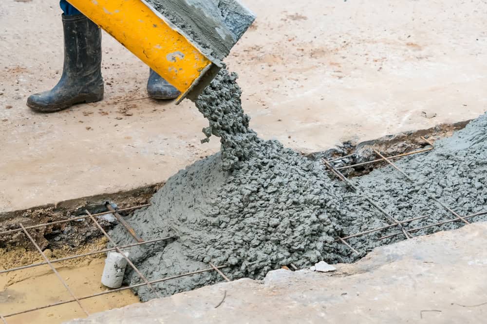 Wet concrete being poured from a yellow chute onto steel reinforcement bars at a construction site
