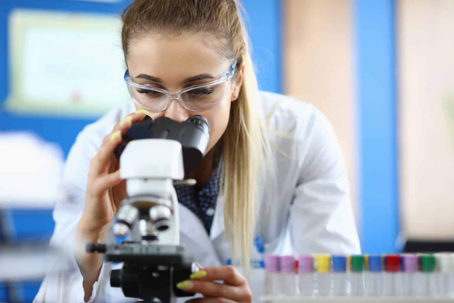 Close-up of laboratory assistant doing analysis of samples. Worker examining dna components in microscope. Test-tubes in stand. Analysis and chemistry concept