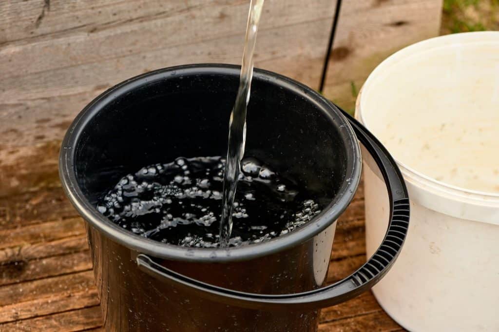 a black plastic bucket is filled with water from the pump