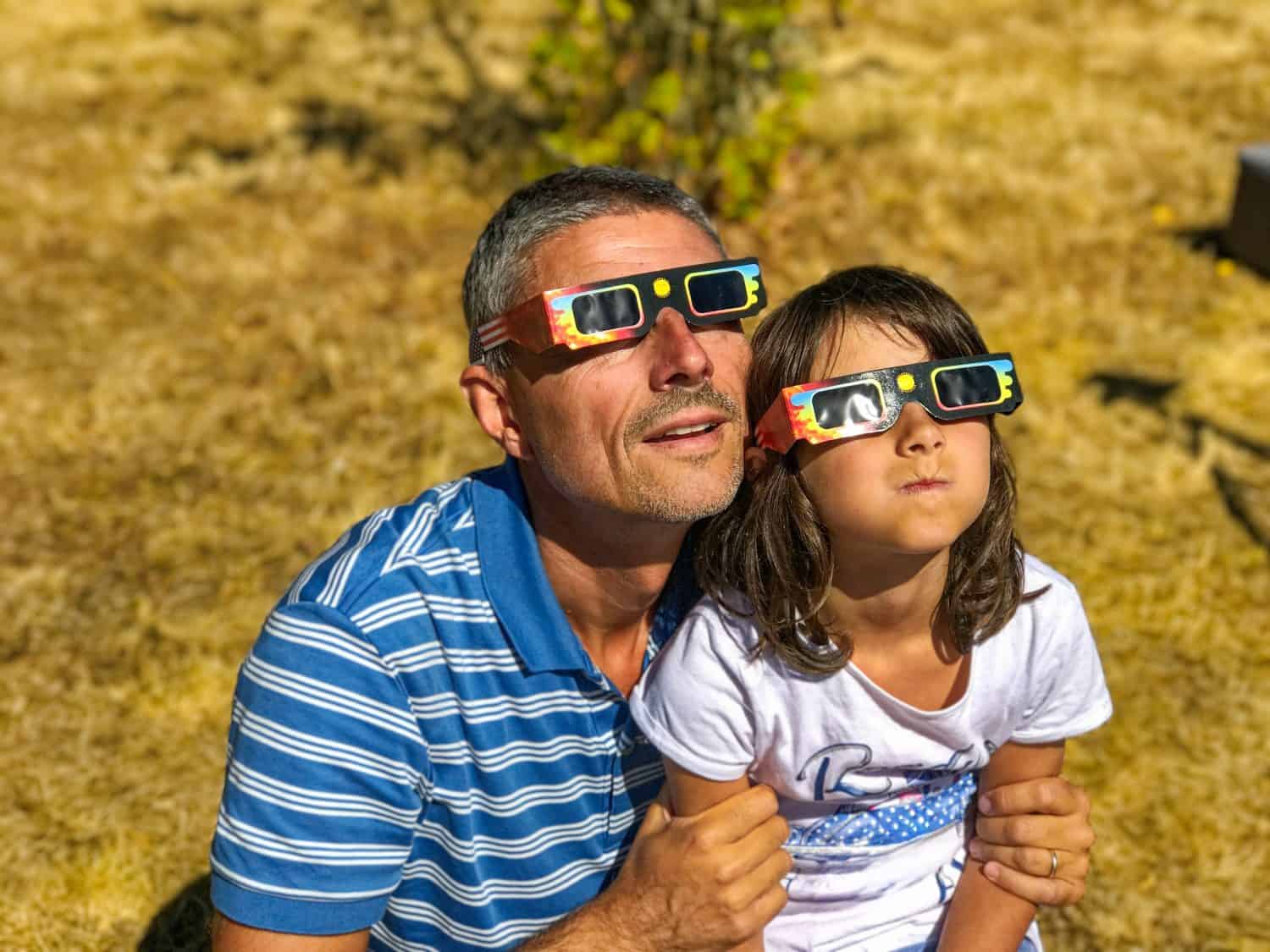 Father and daughter, family viewing solar eclipse with special glasses in a park.