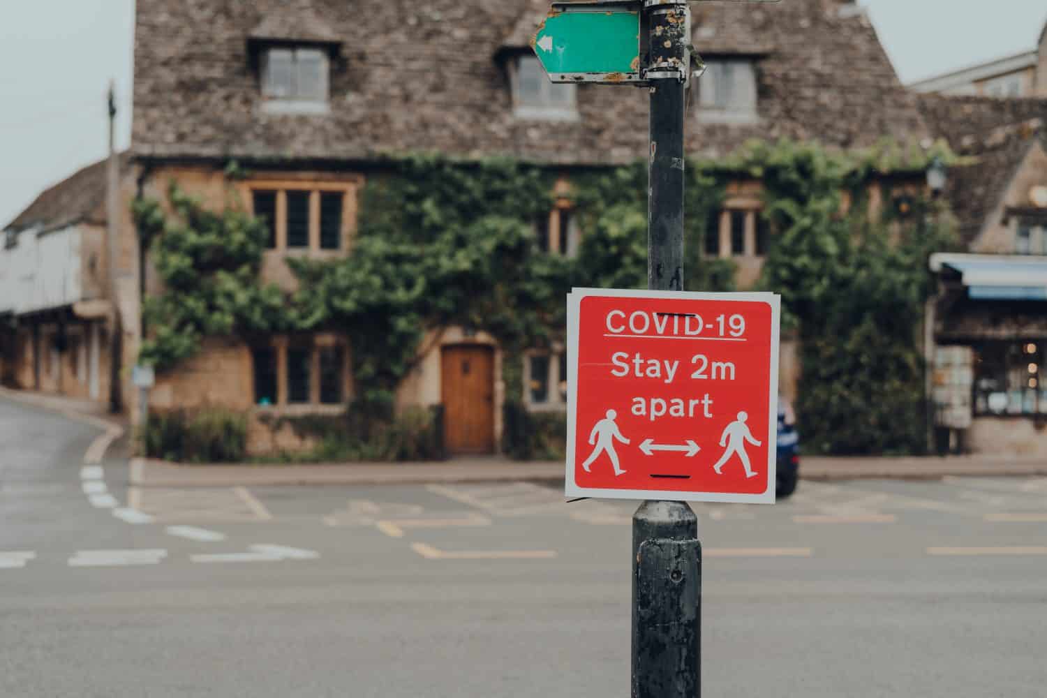 Red Covid-19 Stay 2 Metres Apart warning sign on a street in Bourton-on-Water, Cotswolds, UK, during COVID 19 pandemic. Selective focus.