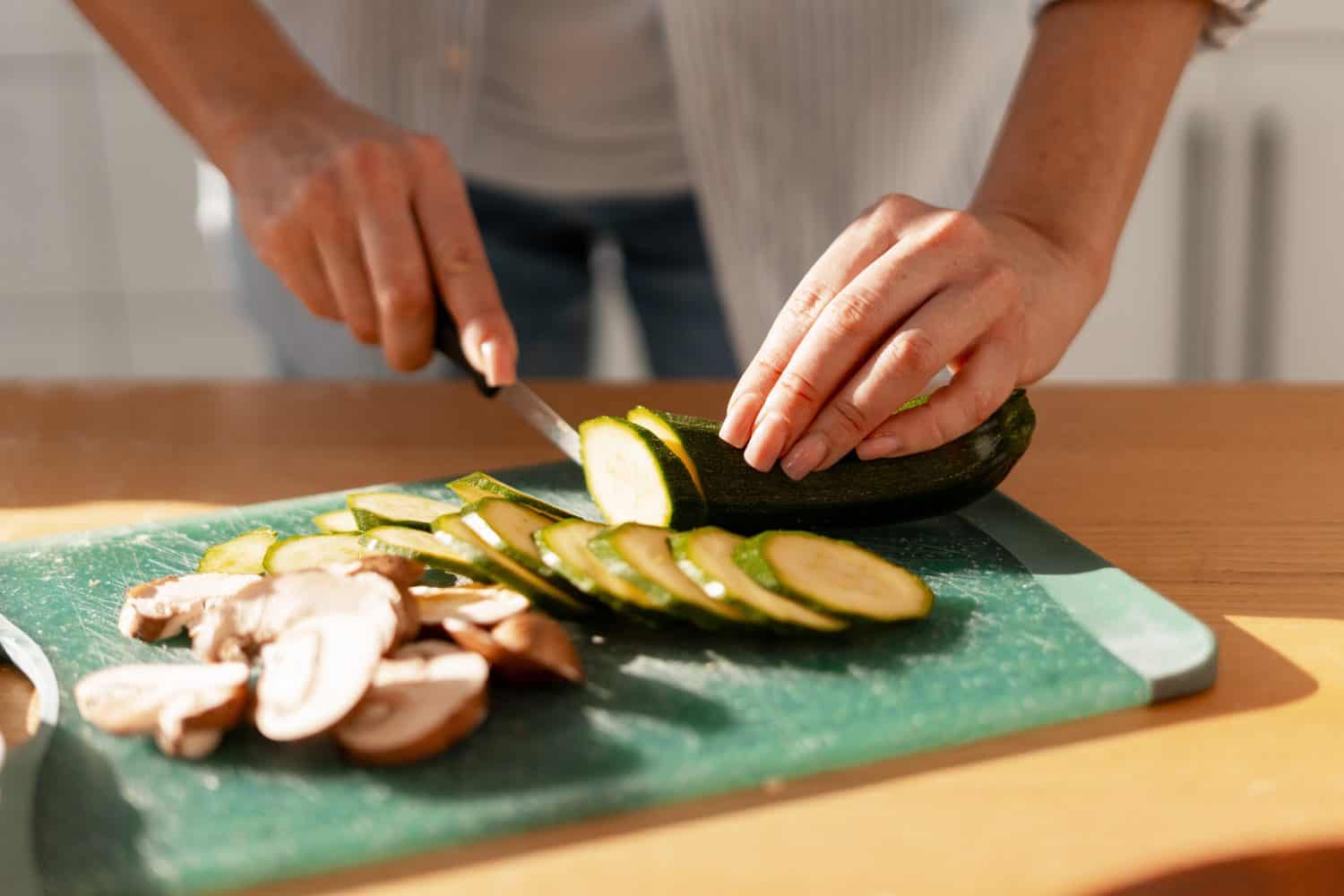 Woman's hands slicing fresh zucchini and mushrooms for meal preparation on a cutting board