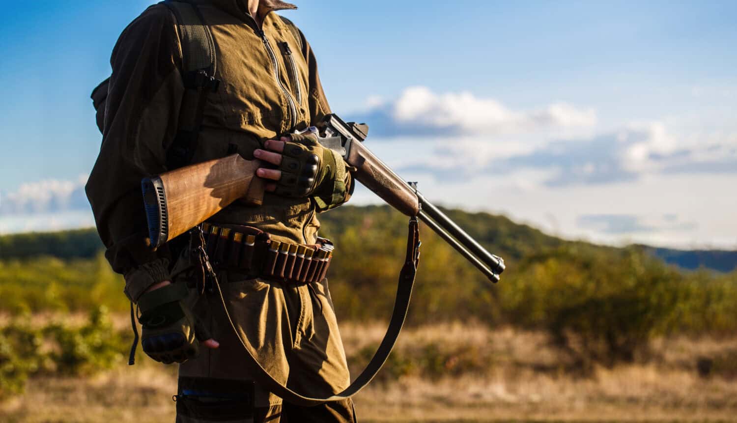 Hunter man. Hunting period, autumn season. Male with a gun. A hunter with a hunting gun and hunting form to hunt in an autumn forest. The man is on the hunt. Hunter with a backpack and a hunting gun. 